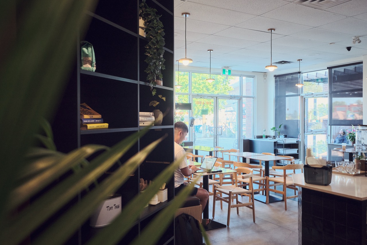 Inside Stucy Cafe, looking past the bookshelf to the wooden tables and front windows.